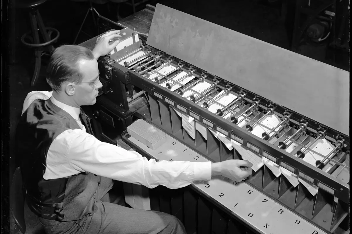 An operator feeds punched cards into a card sorter for a tabulating machine in 1940