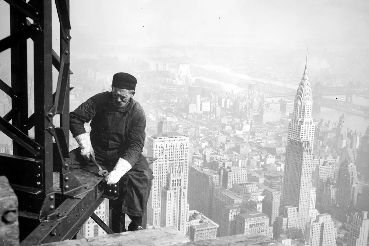 An ironworker on the Empire State Building frame with the Chrysler Building behind